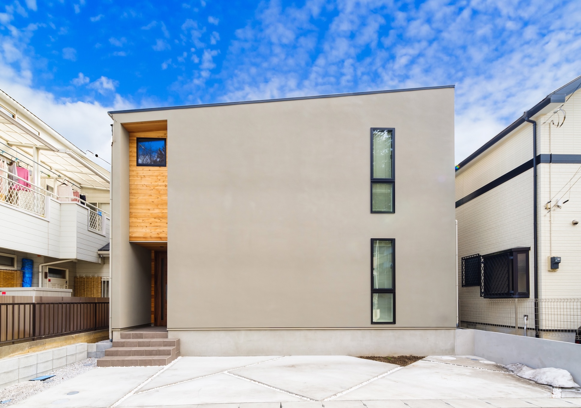 グレーの塗り壁と木調サイディングが調和した外観が特徴です。室内は白を基調とした開放的な空間が広がり、吹抜けからの光が明るく照らします。キッチンとダイニングテーブルは木材で統一され、温かみのある雰囲気を醸し出しています。無駄を削ぎ落としたシンプルなデザインと、機能性を追求した間取りが、快適な居住空間を実現しています。